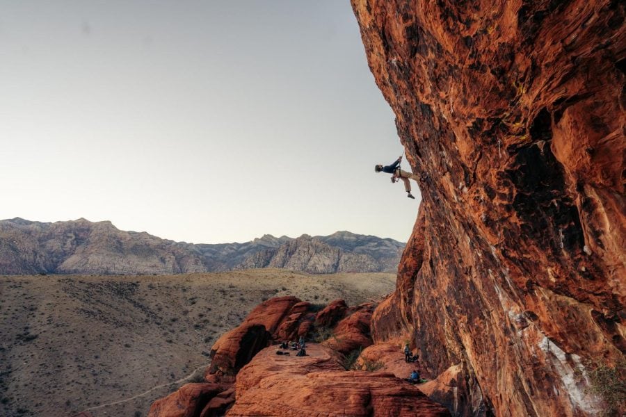 A climber on a red sandstone wall above a desert landscape.