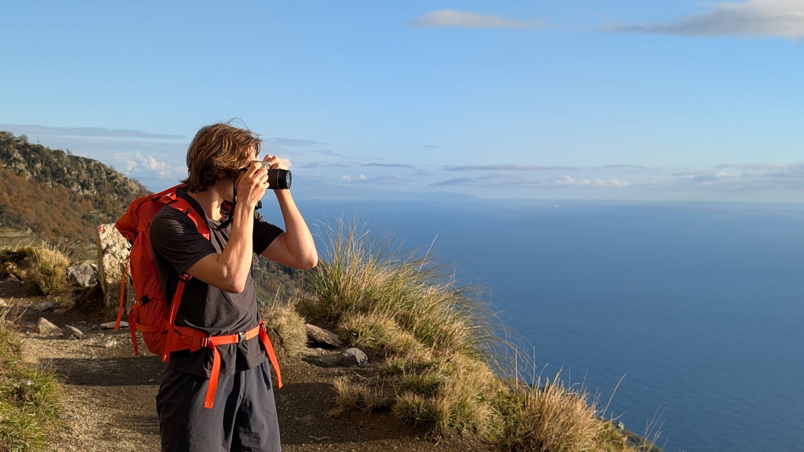 Matteo photographing a blue ocean horizon from a mountain trail.